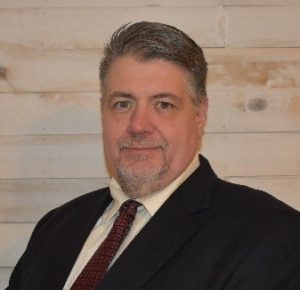 A man in a suit and tie standing in front of a wooden wall.